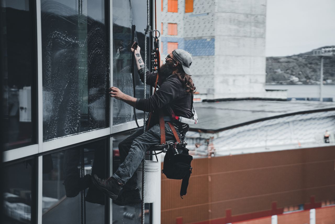 A man cleaning skyscraper windows while wearing a harness, highlighting urban high-rise work.